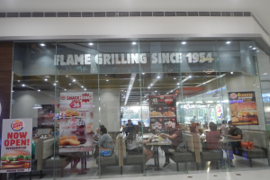 Eine Gruppe von Menschen sitzt an Tischen vor einem Burger King Restaurant mit Glaswänden und Bannern.