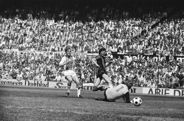 Schwarzes und weißes Foto von Fußballspielern im Einsatz auf einem Feld mit Zuschauern im Hintergrund und einer Bundesliga 1978-79 Ajax 1-1 Hannover 96-Banner.
