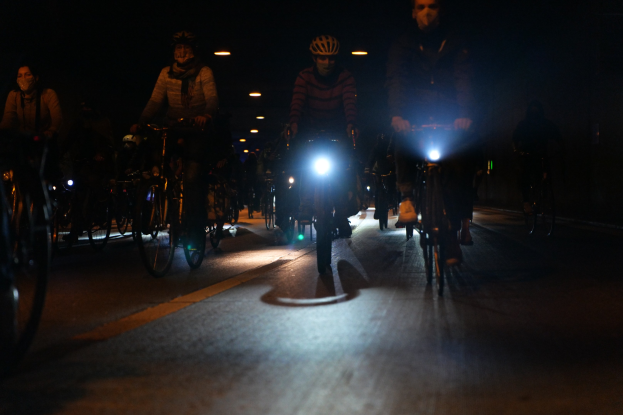 Eine Gruppe von Menschen, die nachts mit Fahrr├Ądern auf einer Stra├če fahren, alle tragen Helme.